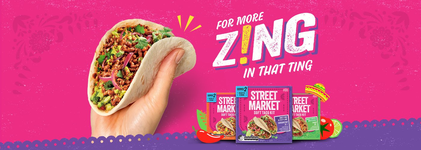 Hand holding a filled taco, with "For more zing in that ting" text and Street Market taco kit boxes on a pink background.